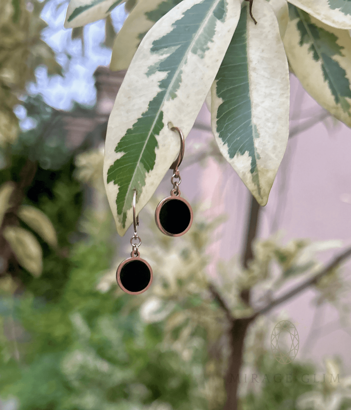 Minimal round hoop inspired drop earrings in black hanging on leaves