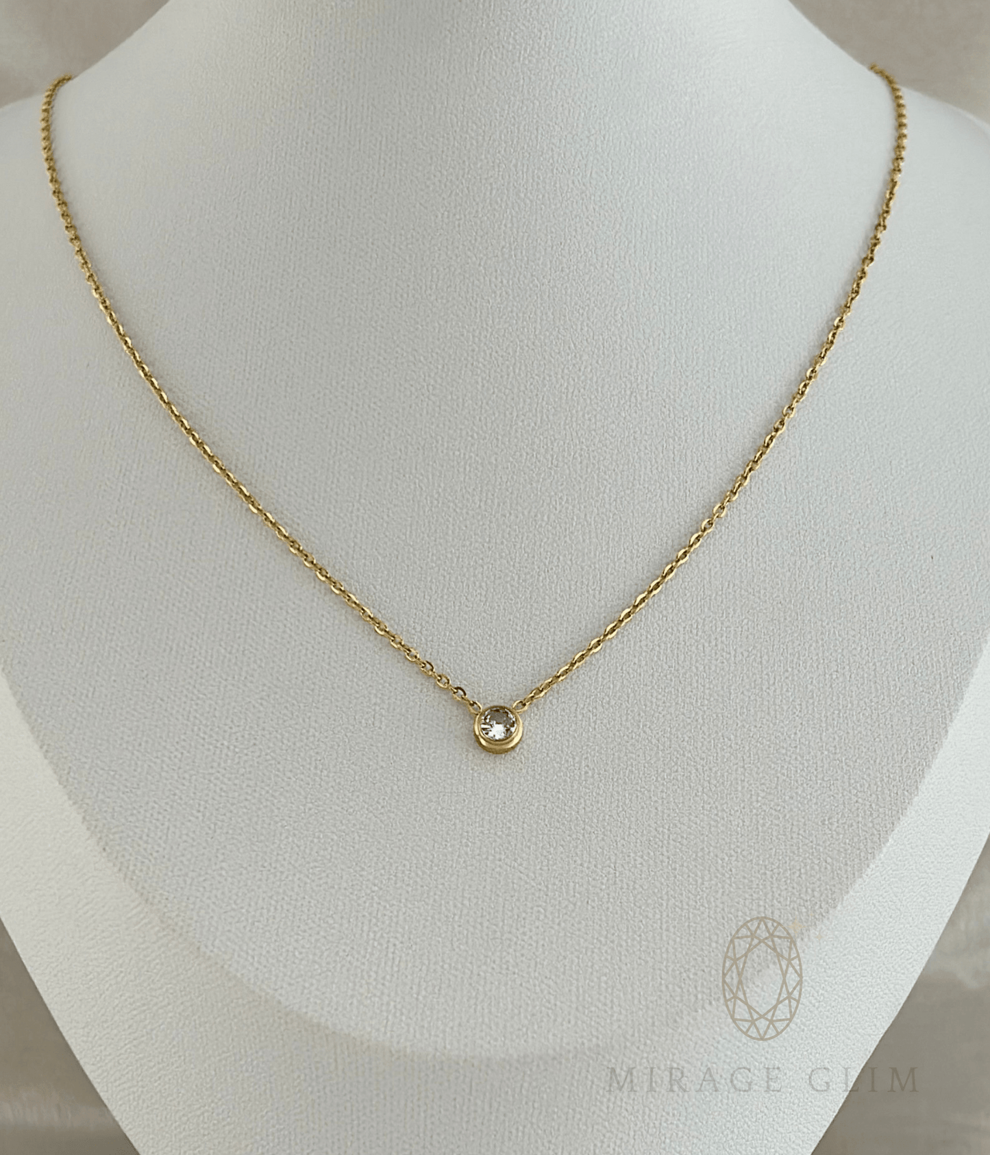 Dainty chain necklace with a circular bezel-set crystal pendant on a white display bust