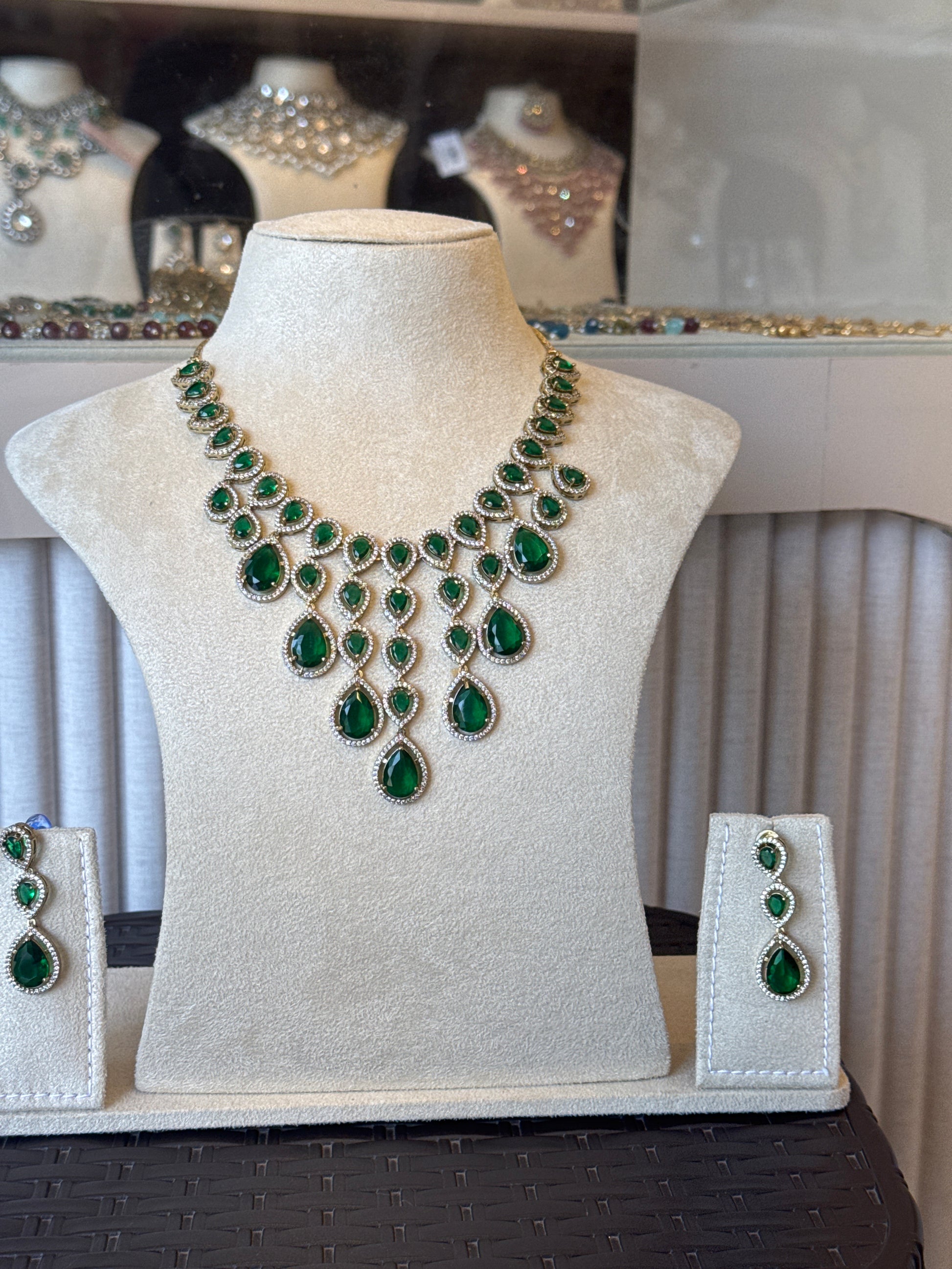Jewelry set with green gemstones on a white cushion against a neutral background