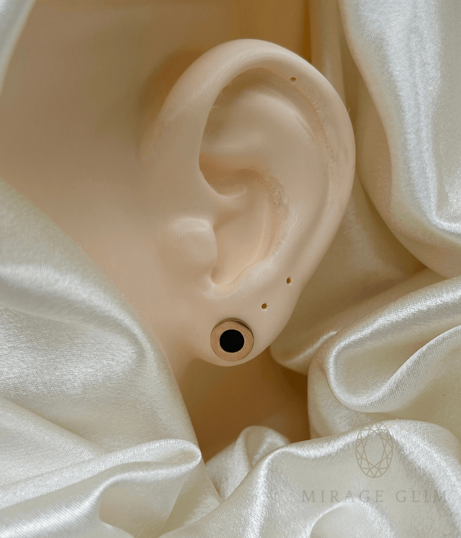 Minimal round stud earring worn on ear with soft satin background