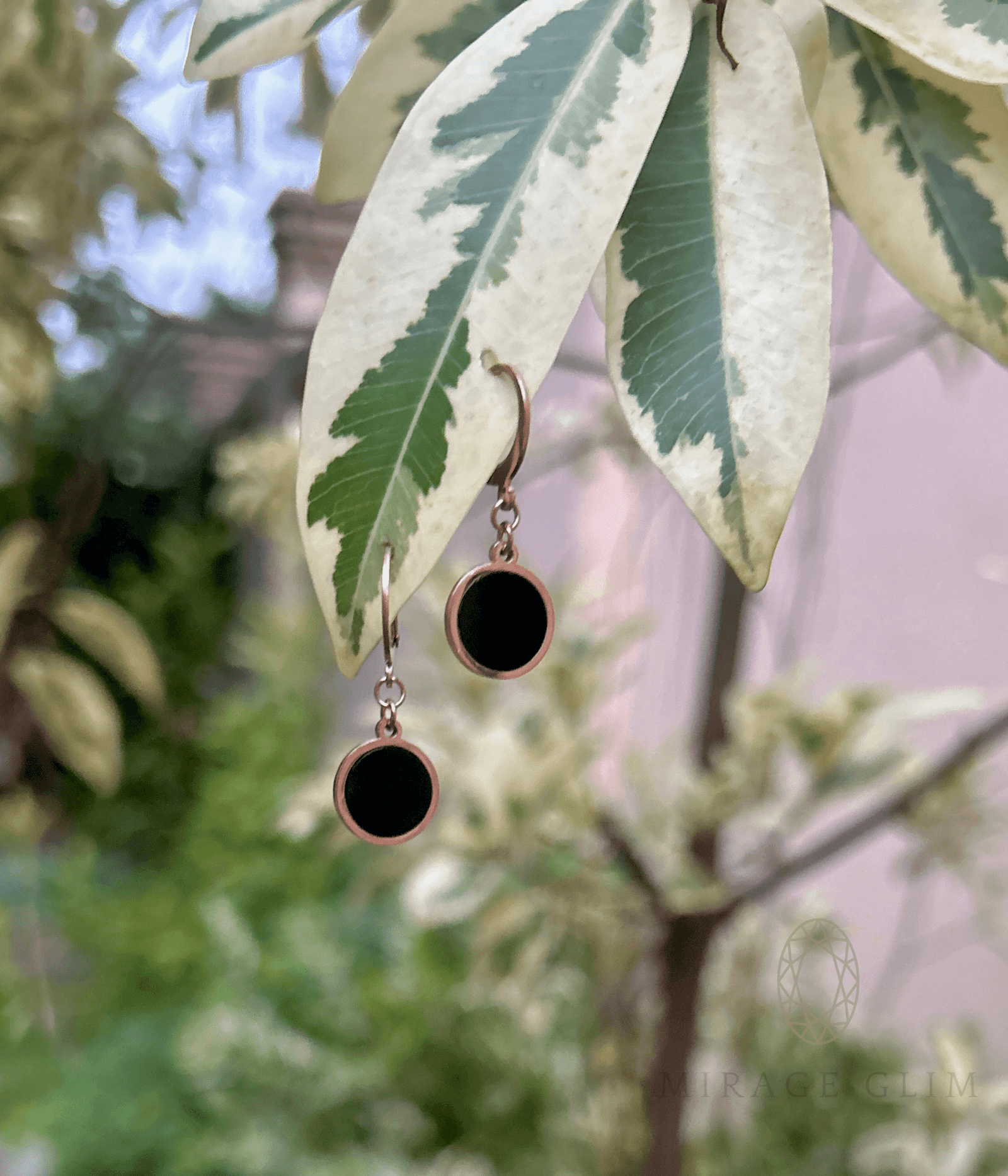 Minimal round hoop inspired drop earrings in black hanging on leaves