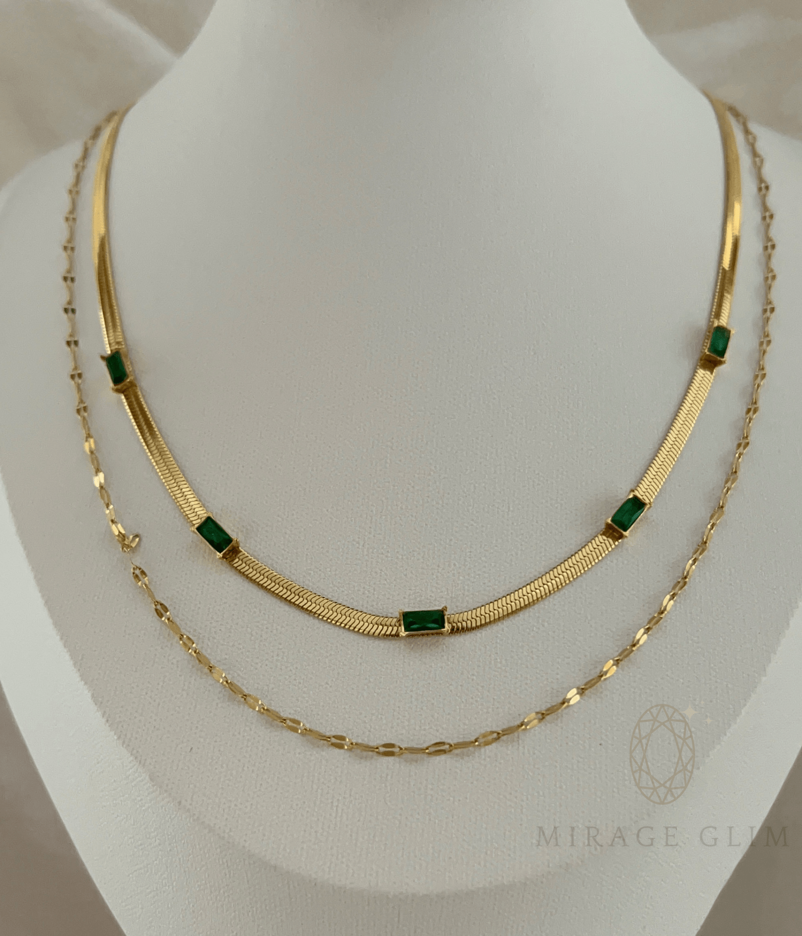 Gold layered necklace with green stone accents on display bust