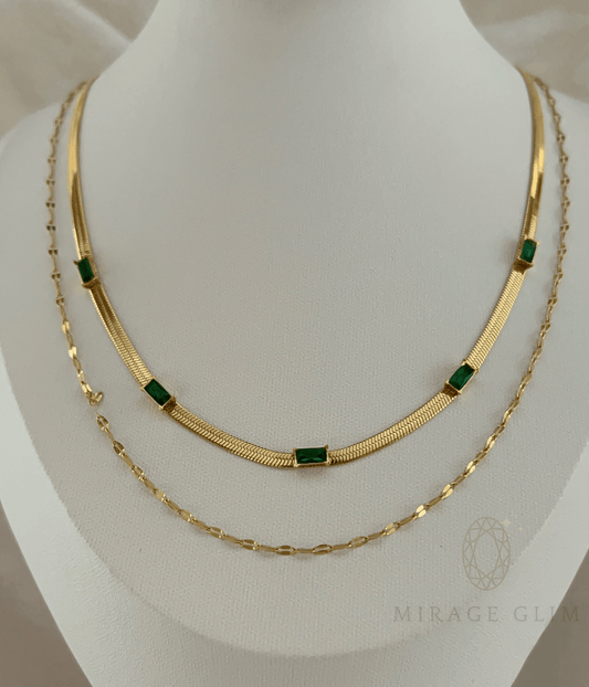 Gold layered necklace with green stone accents on display bust