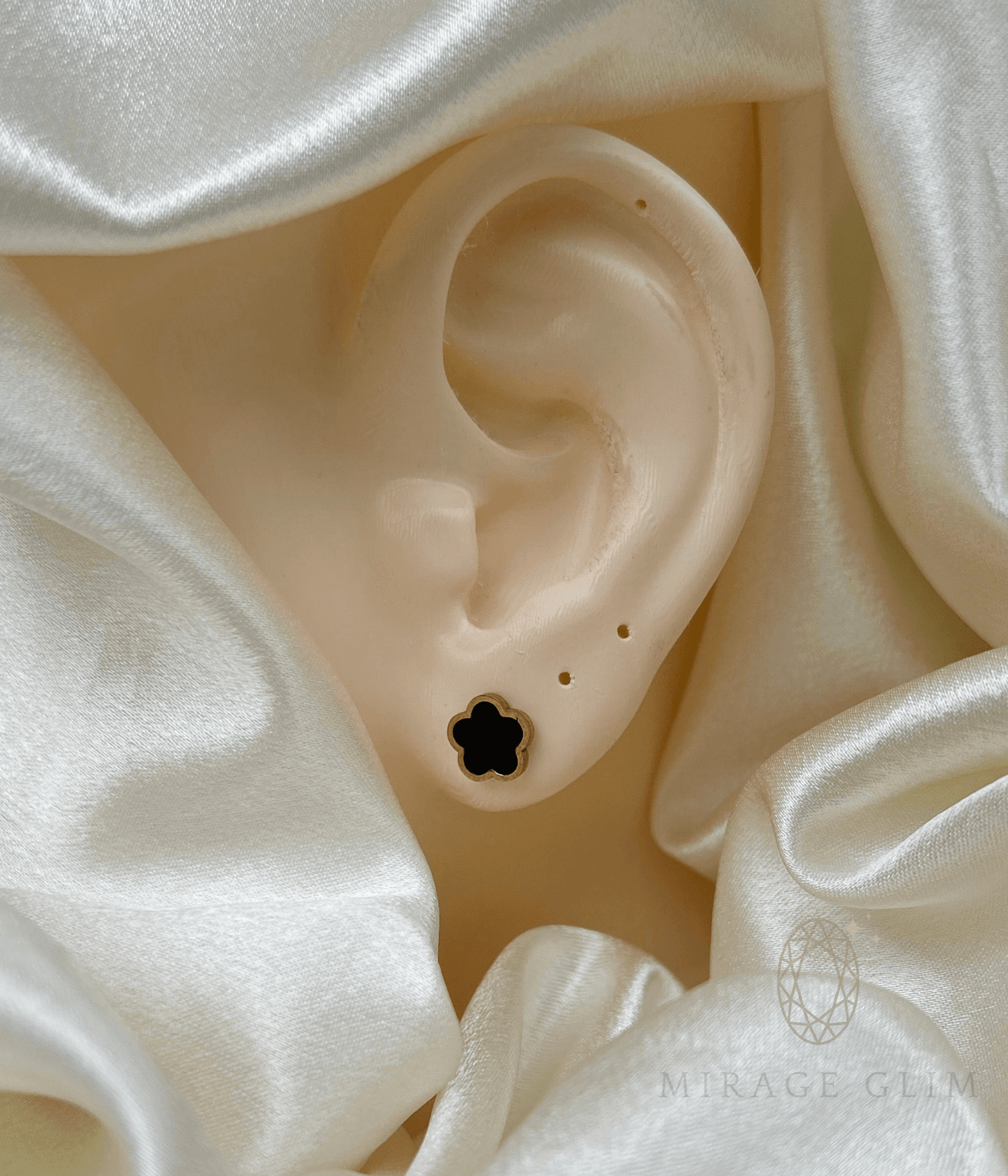 Minimal flower stud earring worn on ear with soft satin background