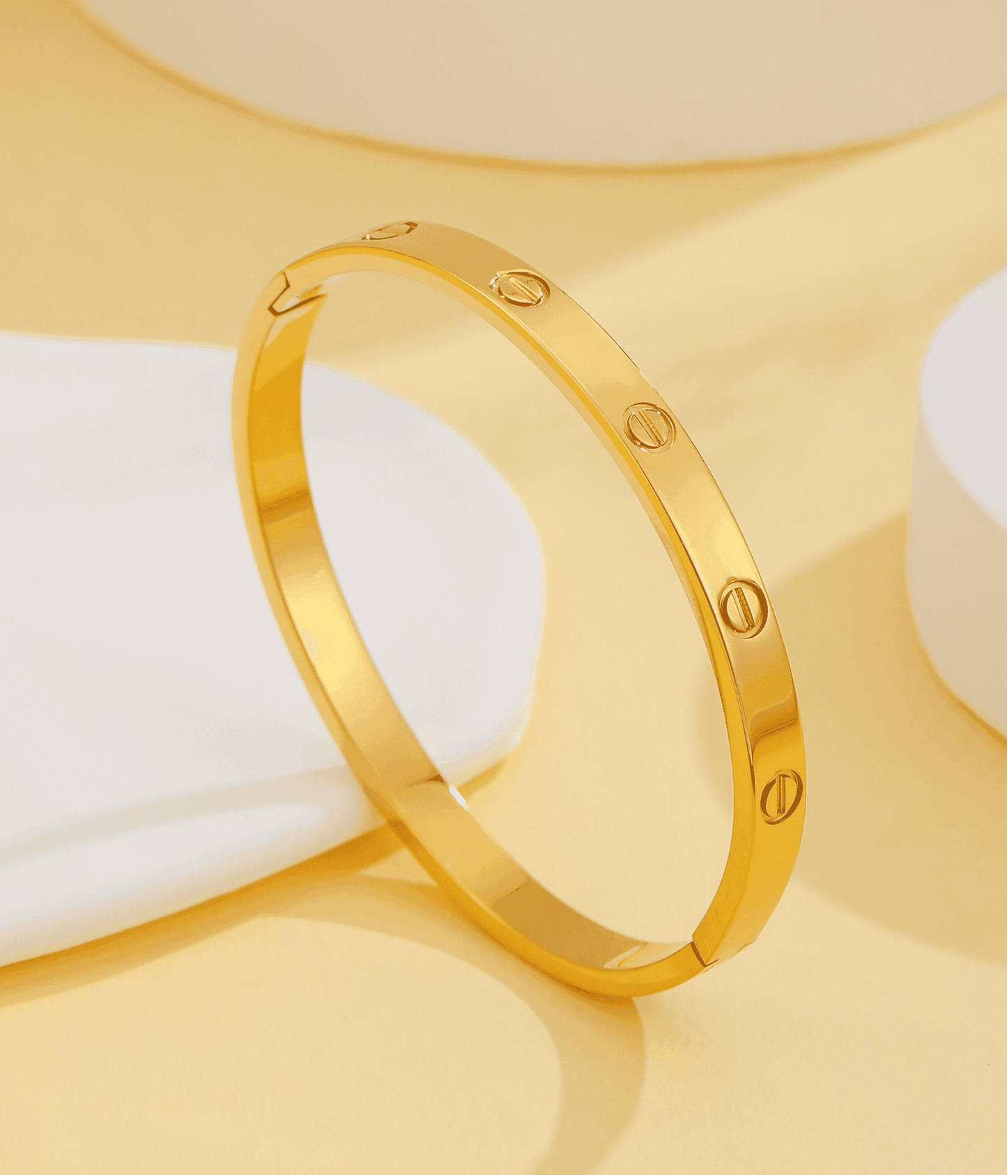 Gold bangle bracelet with engraved screw details on a beige background