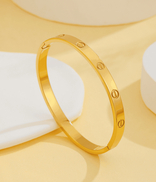 Gold bangle bracelet with engraved screw details on a beige background