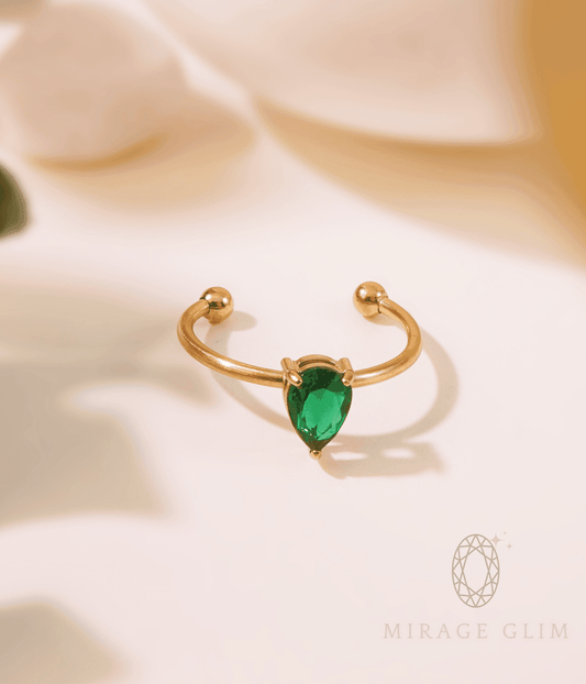 Open gold ring with a teardrop-shaped green stone set at the center, photographed on a soft neutral background