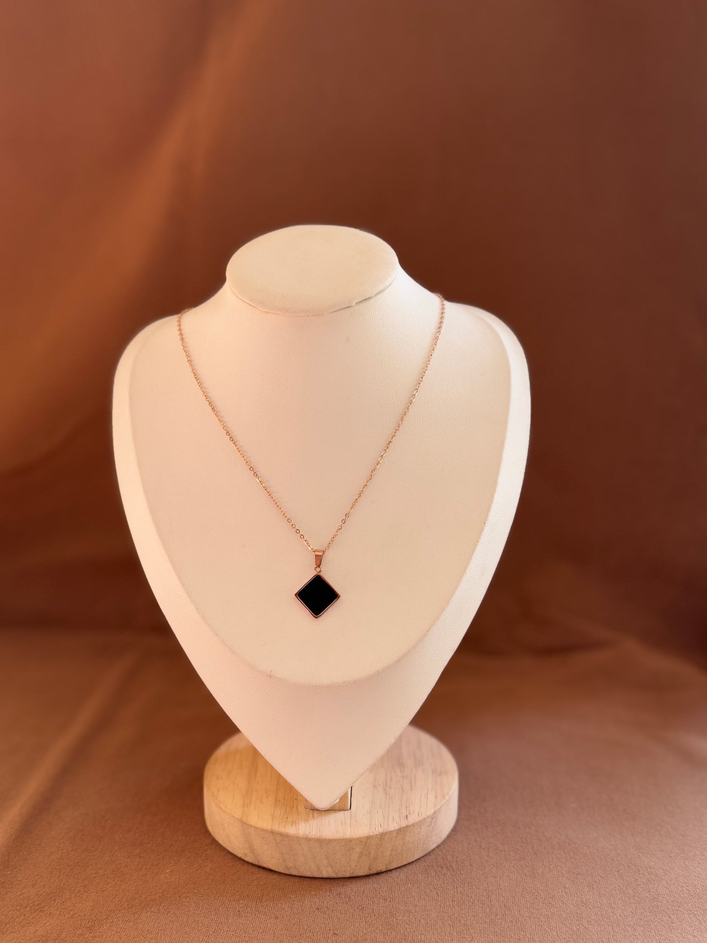 Necklace with a black pendant on a beige mannequin bust against a brown background